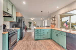 Kitchen with black appliances, decorative light fixtures, light hardwood / wood-style flooring, green cabinetry, and butcher block countertops