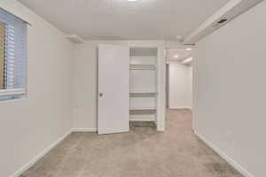 downstairs bedroom with light colored carpet and a textured ceiling