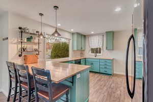 Kitchen featuring wood counters, sink, green cabinetry, light wood-type flooring, and decorative light fixtures