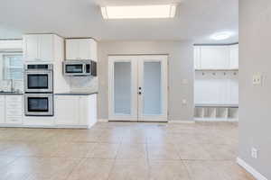 Kitchen with white cabinets, sink, decorative backsplash, light tile patterned floors, and stainless steel appliances