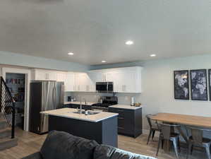 Kitchen featuring white cabinets, a kitchen island with sink, sink, and appliances with stainless steel finishes