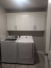 Clothes washing area with cabinets, dark hardwood / wood-style flooring, and washing machine and clothes dryer