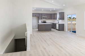 Kitchen with a center island, sink, stainless steel appliances, high vaulted ceiling, and light wood-type flooring