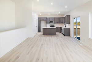 Kitchen featuring stainless steel appliances, sink, light hardwood / wood-style flooring, high vaulted ceiling, and a kitchen island