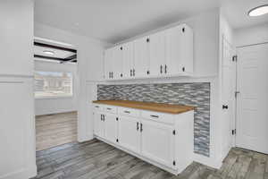 Kitchen featuring wooden counters, decorative backsplash, light wood-type flooring, and white cabinets