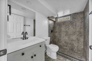 Bathroom featuring a textured ceiling, vanity, tiled shower, tile patterned flooring, and toilet