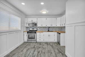 Kitchen with white cabinets, light hardwood / wood-style floors, stainless steel appliances, and wooden counters