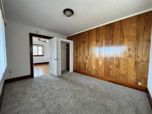 Unfurnished bedroom featuring carpet flooring, wood walls, and ornamental molding