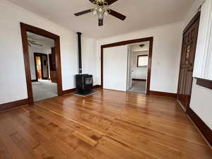 Unfurnished living room featuring a wood stove, ceiling fan, ornamental molding, and hardwood / wood-style flooring