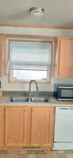 Kitchen with light brown cabinets, white dishwasher, and sink