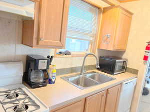 Kitchen featuring sink, black range oven, light brown cabinets, range hood, and white dishwasher