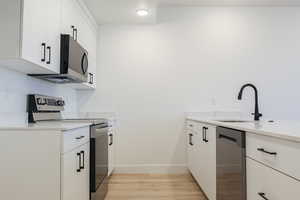 Kitchen with sink, light stone countertops, light wood-type flooring, appliances with stainless steel finishes, and white cabinetry