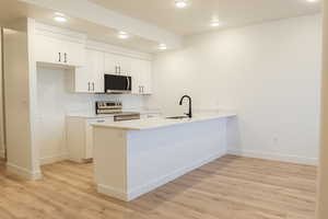 Kitchen featuring kitchen peninsula, appliances with stainless steel finishes, sink, light hardwood / wood-style floors, and white cabinetry