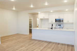 Kitchen featuring white cabinets, sink, light hardwood / wood-style floors, kitchen peninsula, and stainless steel appliances