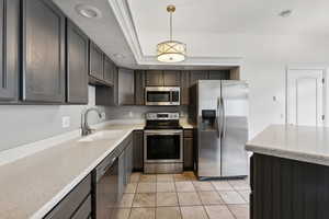 Kitchen featuring sink, light tile patterned floors, appliances with stainless steel finishes, a tray ceiling, and decorative light fixtures