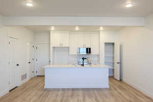 Kitchen with white cabinets, light wood-type flooring, an island with sink, and appliances with stainless steel finishes