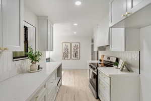 Kitchen with light wood-type flooring, white cabinetry, stainless steel stove, and tasteful backsplash