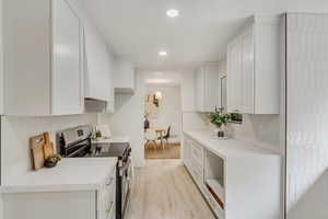 Kitchen with white cabinets, stainless steel stove, light hardwood / wood-style flooring, and tasteful backsplash