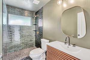 Bathroom featuring a tile shower, vanity, a textured ceiling, and toilet