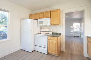 Kitchen with radiator heating unit, white appliances, light hardwood / wood-style flooring, and light brown cabinets