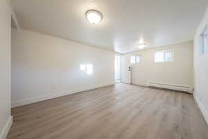 Empty room with a baseboard radiator, a textured ceiling, and light hardwood / wood-style floors