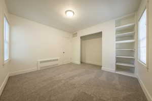 Unfurnished bedroom with carpet flooring, radiator heating unit, and a closet