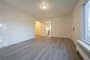 Unfurnished room with radiator heating unit, light wood-type flooring, and plenty of natural light