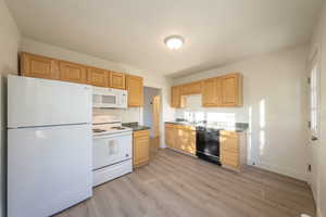 Kitchen featuring light brown cabinetry, white appliances, light hardwood / wood-style flooring, and sink