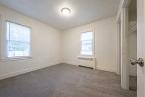 Unfurnished bedroom with carpet, a textured ceiling, and radiator