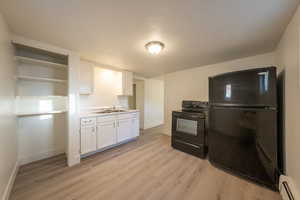 Kitchen with sink, black appliances, a baseboard radiator, light hardwood / wood-style floors, and white cabinetry