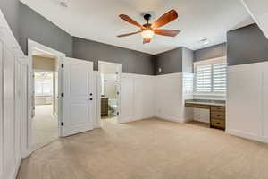 Unfurnished bedroom featuring light carpet, connected bathroom, multiple windows, and built in desk