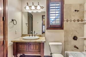 Full bathroom with vanity, tiled shower / bath combo, and toilet