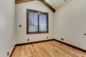 Unfurnished room featuring vaulted ceiling with beams and light hardwood / wood-style flooring