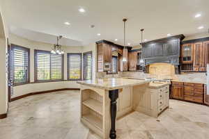 Kitchen featuring a kitchen island with sink, hanging light fixtures, a kitchen breakfast bar, light stone counters, and decorative backsplash