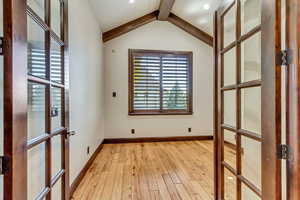 Empty room featuring vaulted ceiling with beams and light hardwood / wood-style floors