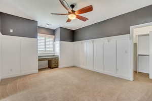 Interior space with ceiling fan, light colored carpet, and built in desk