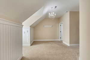 Additional living space featuring a chandelier, light colored carpet, and vaulted ceiling