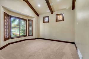 Carpeted empty room featuring vaulted ceiling with beams