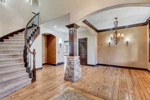 Entrance foyer featuring light wood-type flooring, decorative columns, a textured ceiling, crown molding, and an inviting chandelier