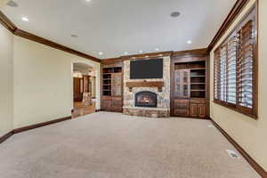 Unfurnished living room with carpet flooring, a stone fireplace, crown molding, and built in shelves