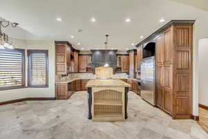 Kitchen with pendant lighting, a center island, built in appliances, tasteful backsplash, and light stone counters