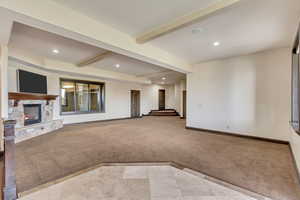 Unfurnished living room with a stone fireplace, light colored carpet, and beam ceiling