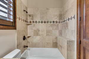 Bathroom featuring tiled shower / bath combo and toilet