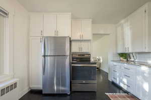 Kitchen with decorative backsplash, light stone counters, stainless steel appliances, white cabinets, and radiator heating unit