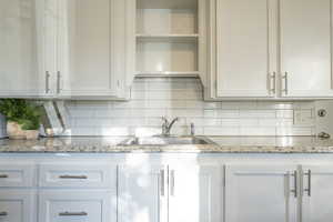 Kitchen featuring decorative backsplash, light stone counters, white cabinetry, and sink