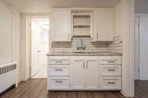 Kitchen with radiator heating unit, tasteful backsplash, white cabinetry, and dark wood-type flooring