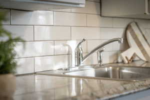 Interior details featuring light stone countertops, decorative backsplash, and sink