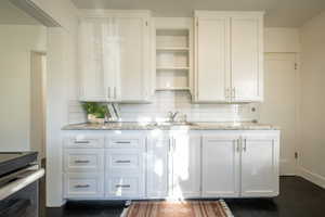 Interior space featuring white cabinets, backsplash, light stone counters, and sink