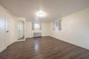 Basement with a textured ceiling, radiator, and dark hardwood / wood-style floors