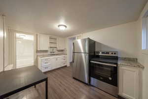 Kitchen featuring light stone countertops, a textured ceiling, dark hardwood / wood-style flooring, white cabinetry, and stainless steel appliances